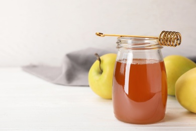 Photo of Jar of honey, apples and dipper on wooden table