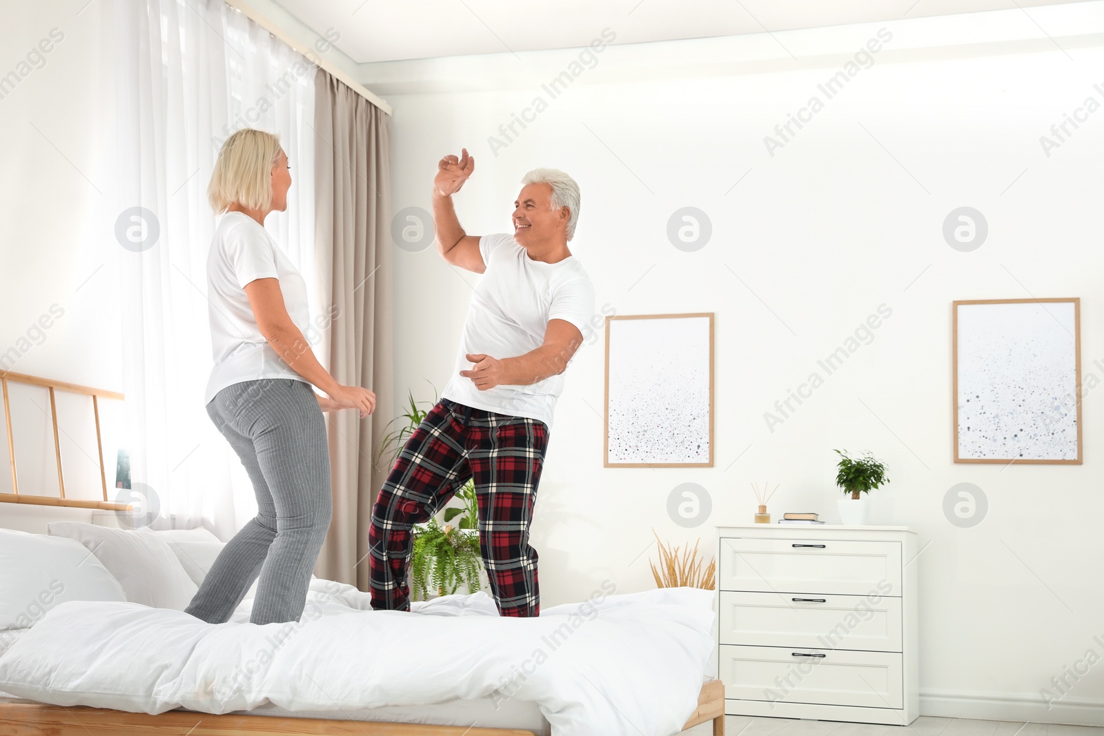 Photo of Happy mature couple dancing together on bed at home