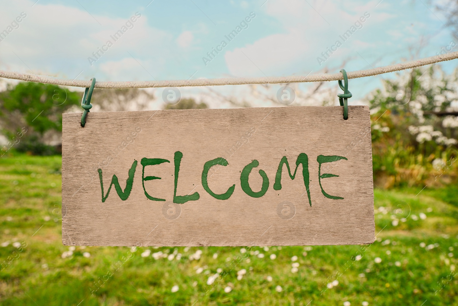 Image of Welcome card. Wooden board with word hanging on rope in countryside