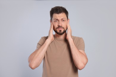 Man suffering from ear pain on grey background