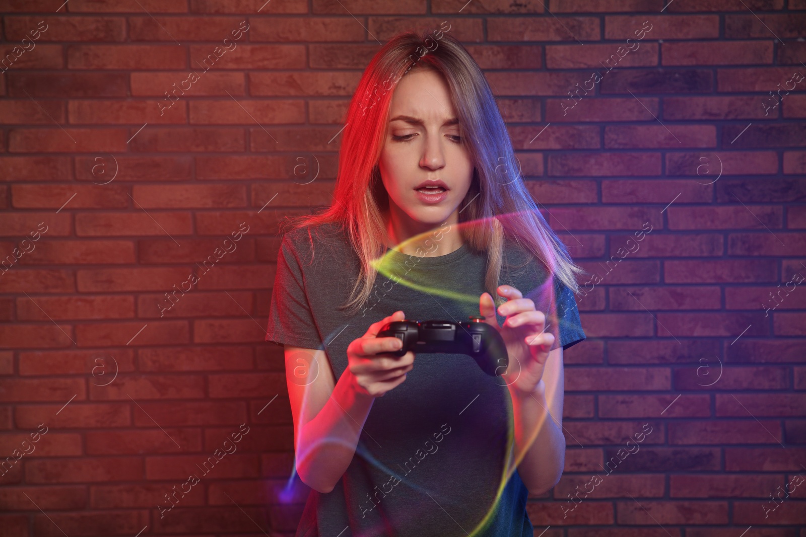 Photo of Emotional young woman playing video games with controller near brick wall