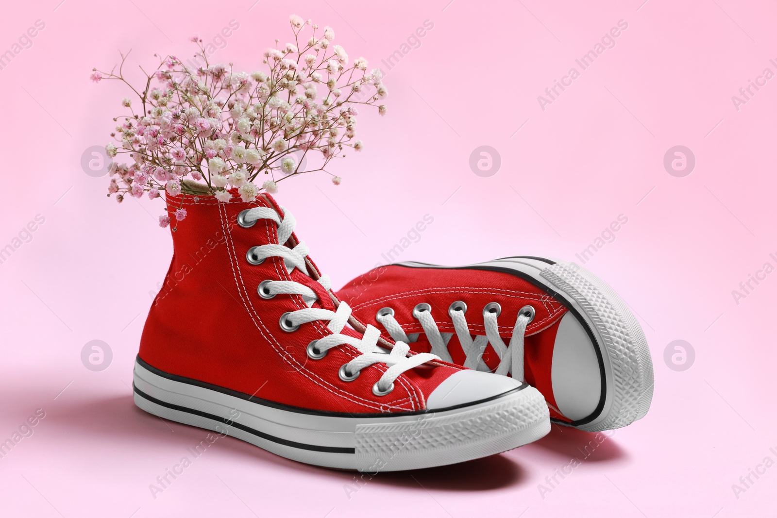 Photo of Pair of new stylish red sneakers with gypsophila flowers on pink background