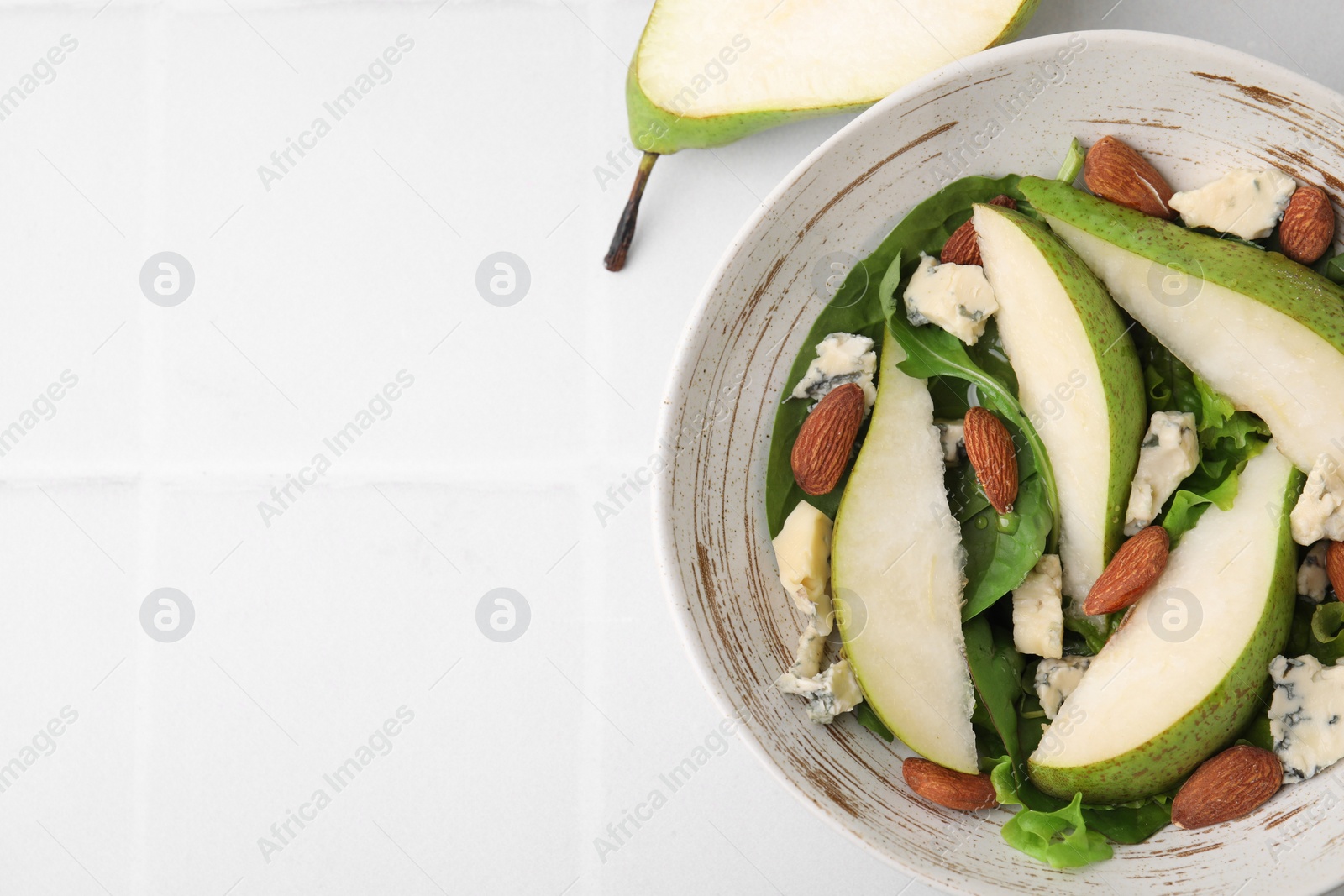 Photo of Delicious pear salad in bowl and fruit on light tiled table, top view. Space for text