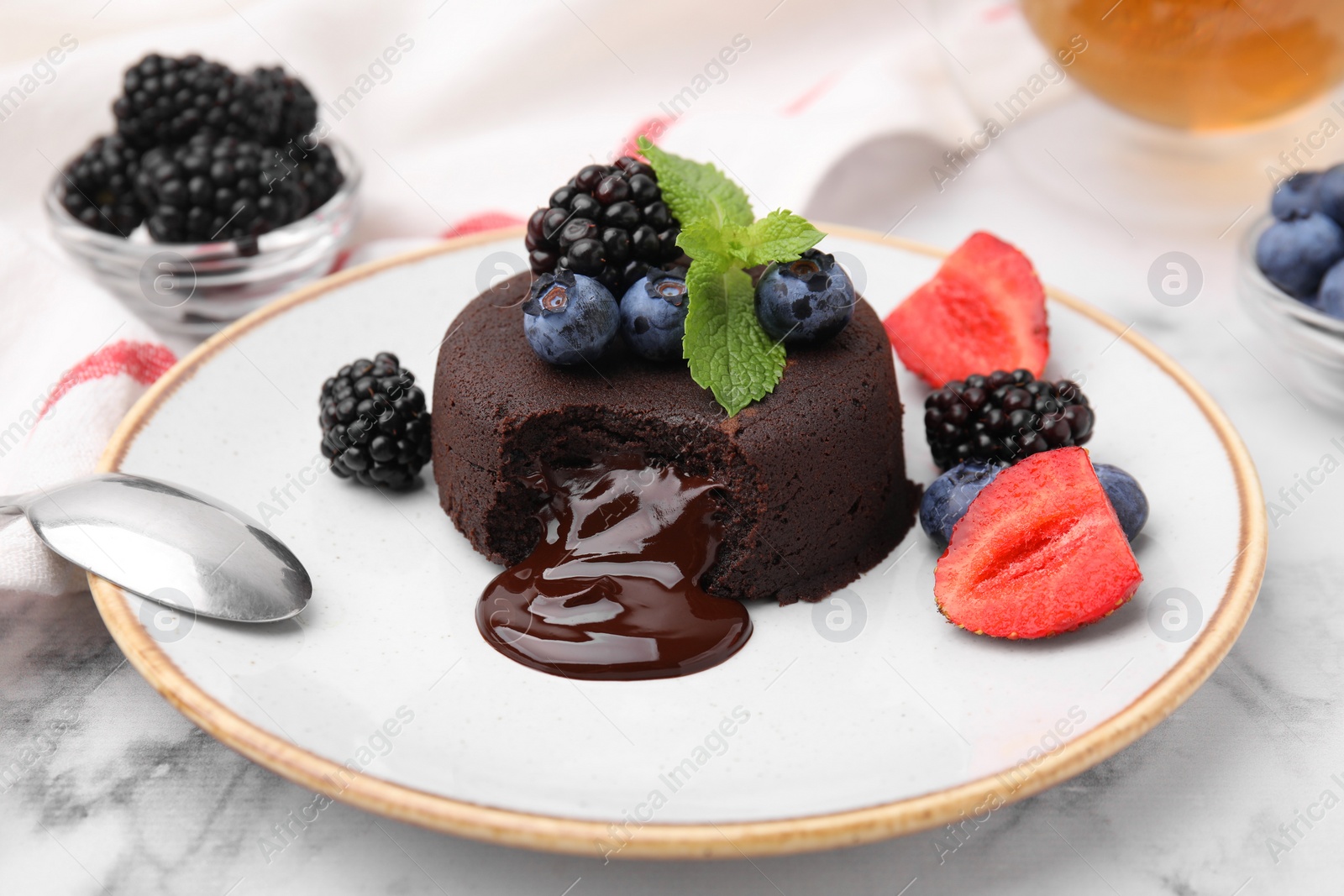 Photo of Plate with delicious chocolate fondant, berries and mint on white marble table, closeup