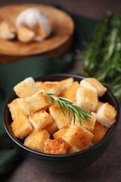 Photo of Delicious crispy croutons and rosemary in bowl on dark table, closeup