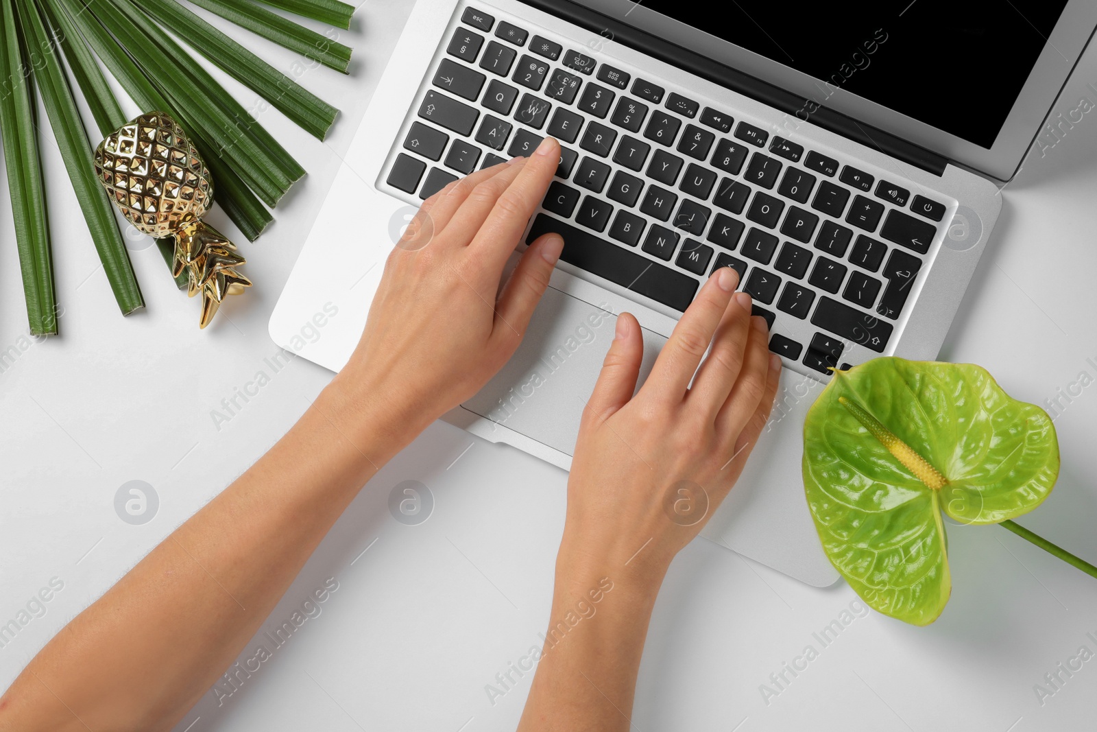 Photo of Woman using laptop on white table decorated with tropical flower, top view. Creative design ideas