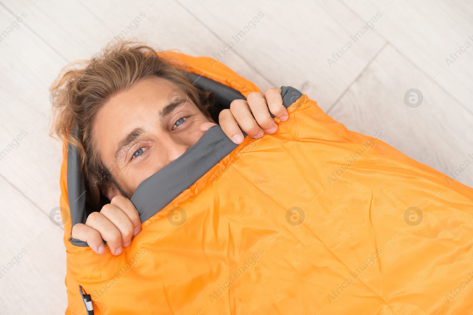 Photo of Young man in comfortable sleeping bag on floor, top view