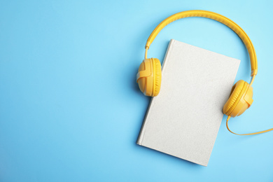 Photo of Book and modern headphones on light blue background, top view. Space for text