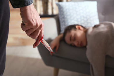 Photo of Man with bloody knife and his victim on couch indoors, closeup. Dangerous criminal