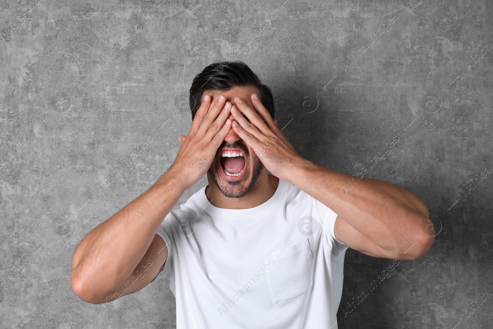 Photo of Young man being blinded and covering eyes with hands on grey background