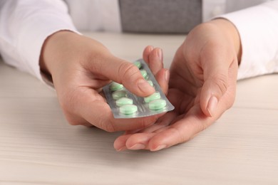 Woman holding blister of green pills at white wooden table, closeup