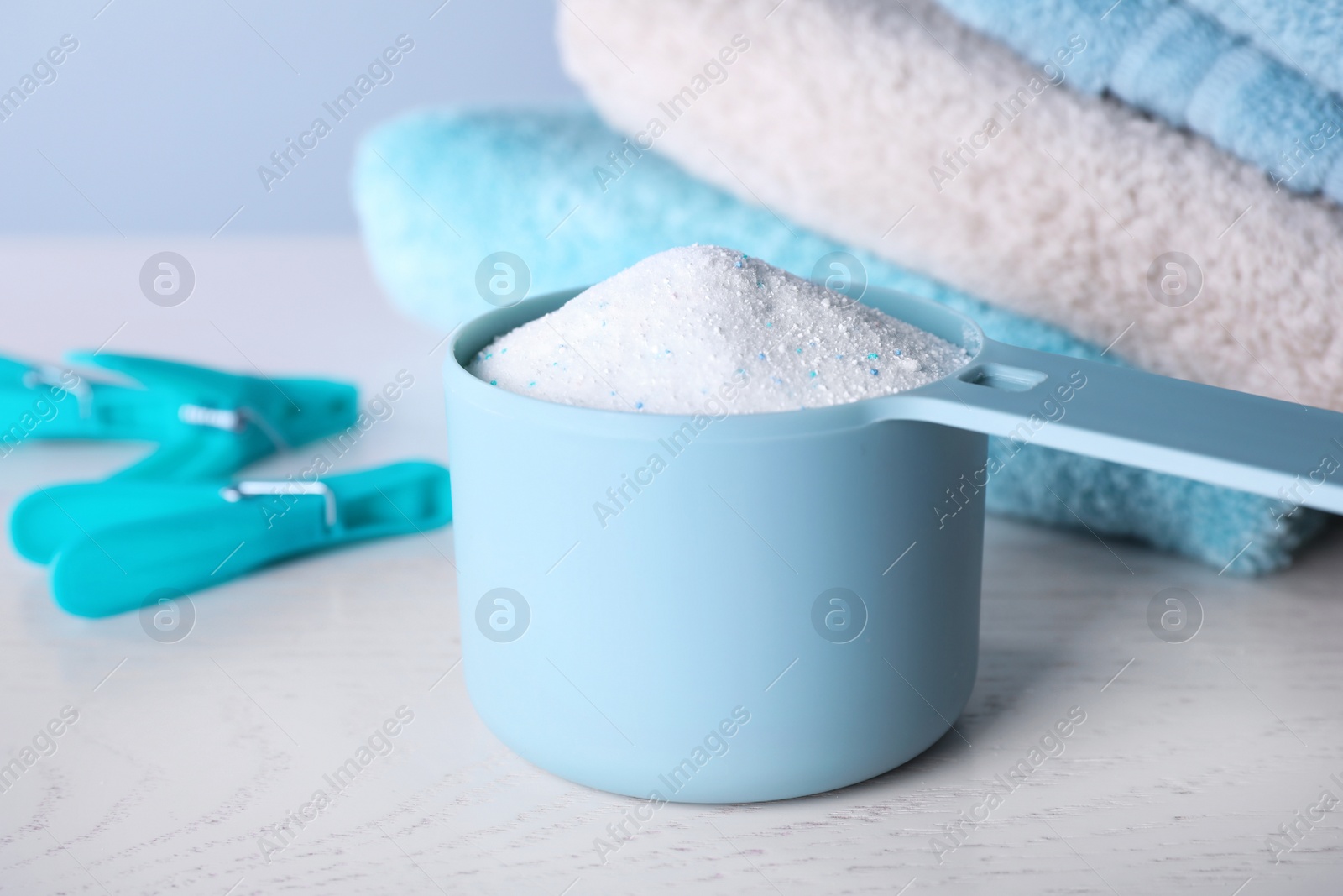 Photo of Measuring spoon of laundry powder near towels and clothespins on table