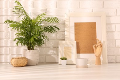 Photo of Stylish office workplace. Decor elements, plants and cup on white table near brick wall