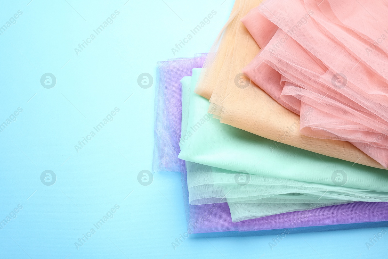 Photo of Beautiful colorful tulle fabrics on turquoise background. Space for text