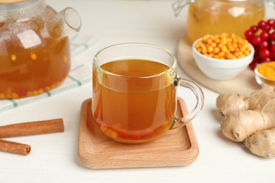 Photo of Glass cup of immunity boosting tea with ingredients on white wooden table