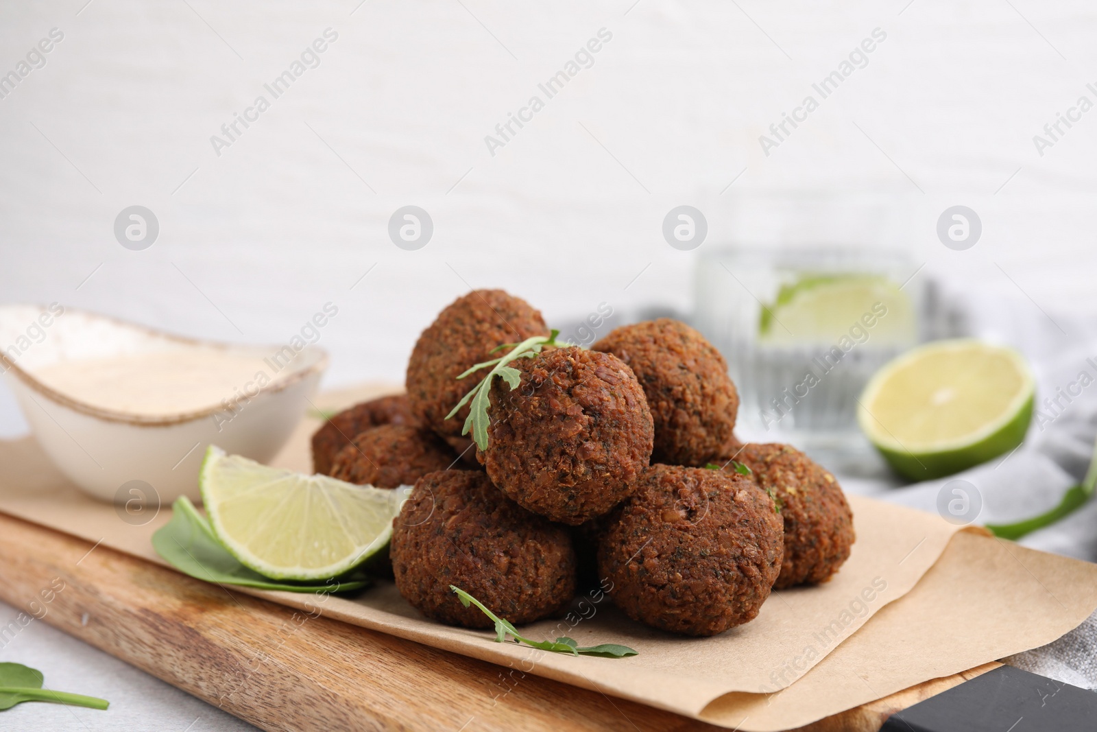 Photo of Delicious falafel balls, arugula, lime and sauce on table