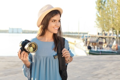 Young female photographer holding professional camera at pier. Space for text