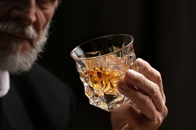 Man holding glass of whiskey with ice cubes on dark background, closeup