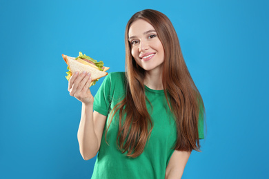 Young woman with tasty sandwich on light blue background