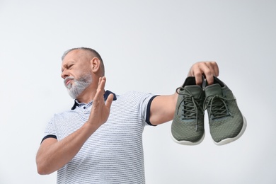 Man feeling bad smell from shoes on white background. Air freshener