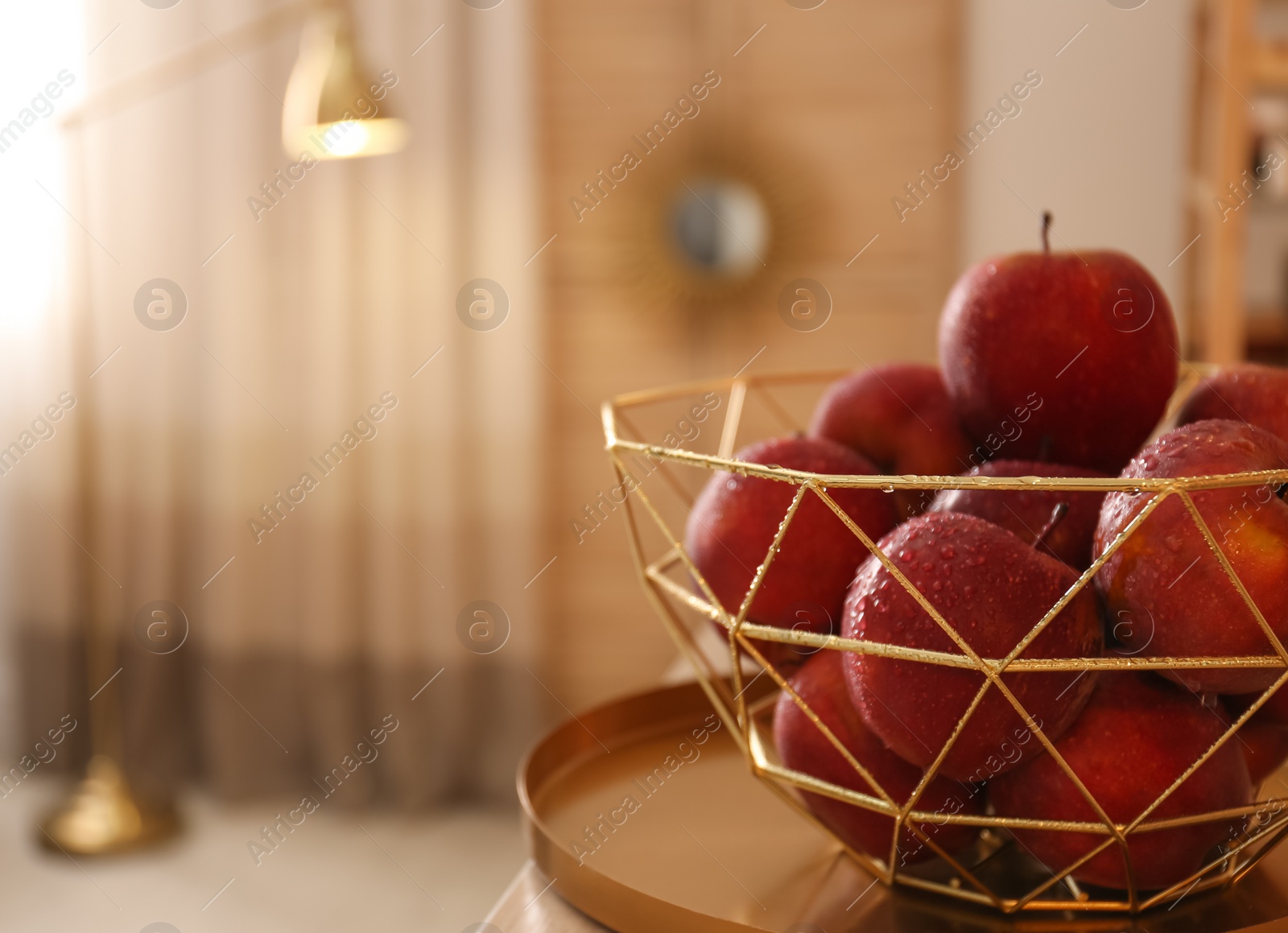 Photo of Fresh ripe red apples with water drops in decorative basket on table indoors, space for text