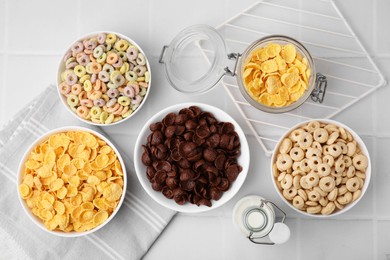 Photo of Different delicious breakfast cereals and milk on white tiled table, flat lay