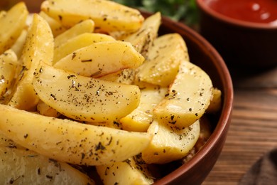 Photo of Bowl with tasty baked potato wedges and spices on wooden table, closeup