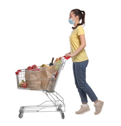 Photo of Woman with protective mask and shopping cart full of groceries on white background