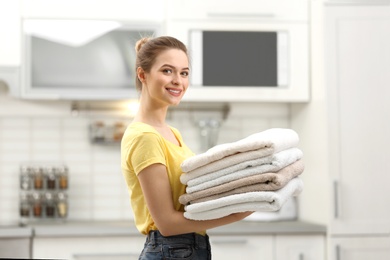 Woman holding folded clean towels in kitchen. Laundry day