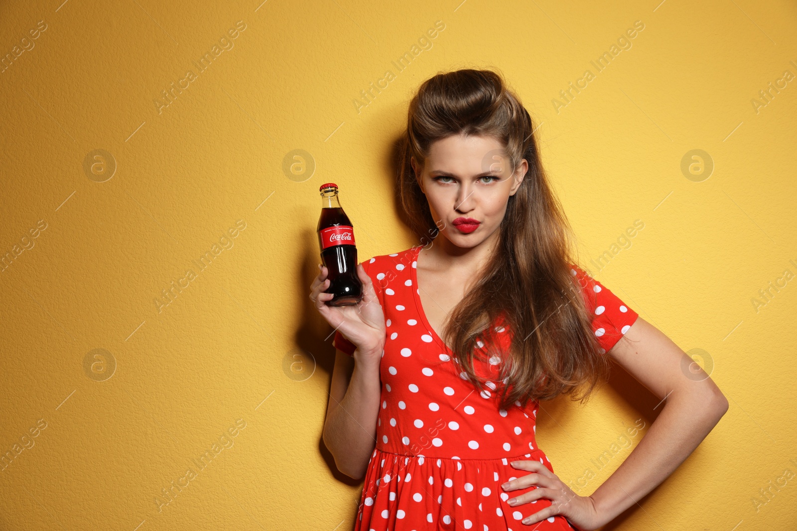 Photo of MYKOLAIV, UKRAINE - NOVEMBER 28, 2018: Young woman with bottle of Coca-Cola on color background