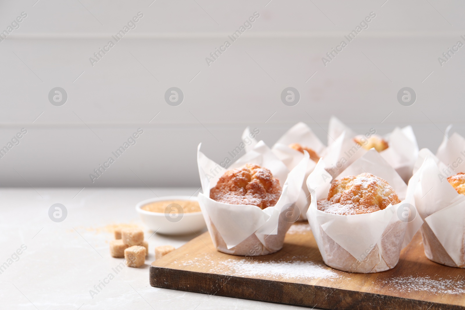 Photo of Delicious muffins with powdered sugar on light table. Space for text