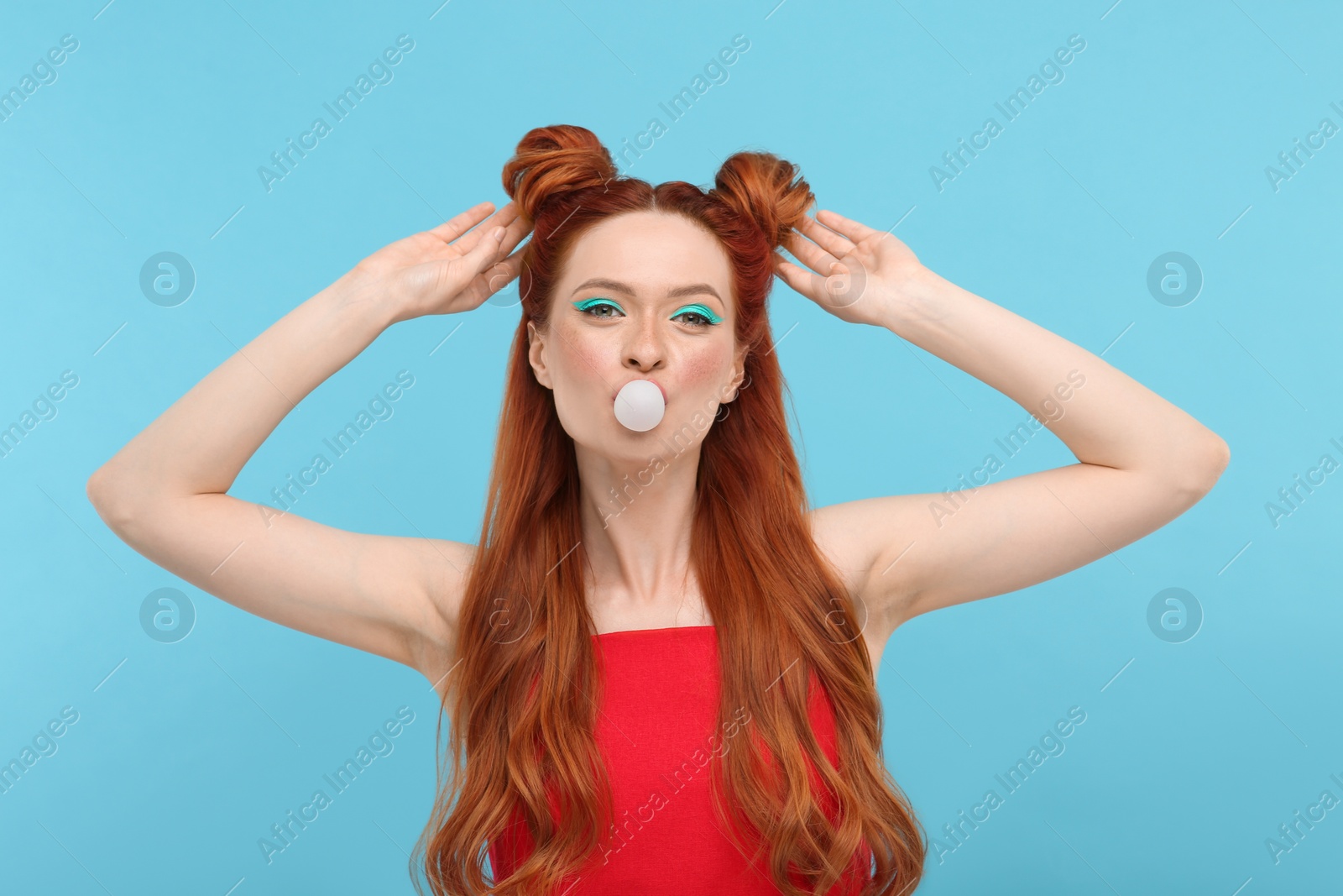 Photo of Portrait of beautiful woman with bright makeup blowing bubble gum on light blue background