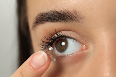 Photo of Woman putting contact lens in her eye on blurred background, closeup