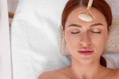 Photo of Young woman receiving facial massage with jade roller in beauty salon, top view. Space for text