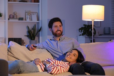 Happy couple watching TV on sofa at home