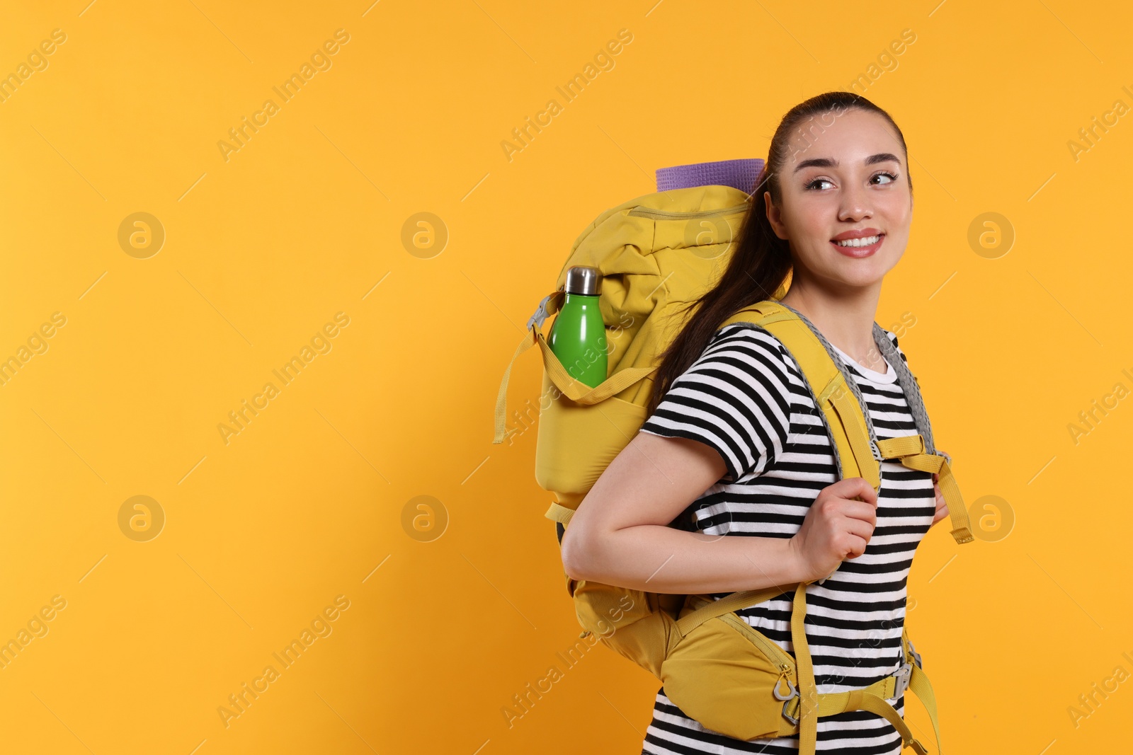 Photo of Smiling young woman with backpack on orange background, space for text. Active tourism