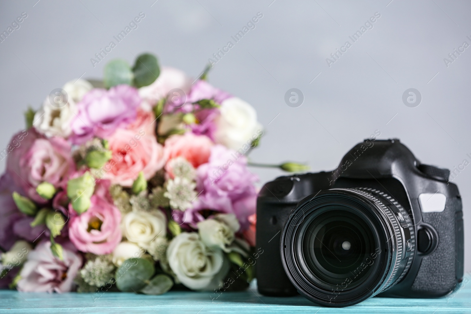 Photo of Modern camera and bouquet on light blue wooden table. International Photographer's day