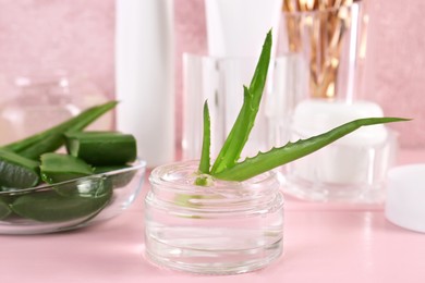 Photo of Jar of natural gel and aloe vera leaves on pink table, closeup