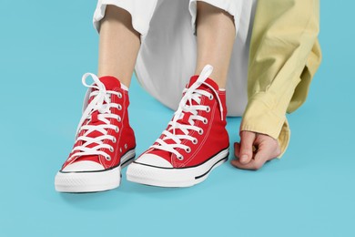 Woman in stylish gumshoes on light blue background, closeup