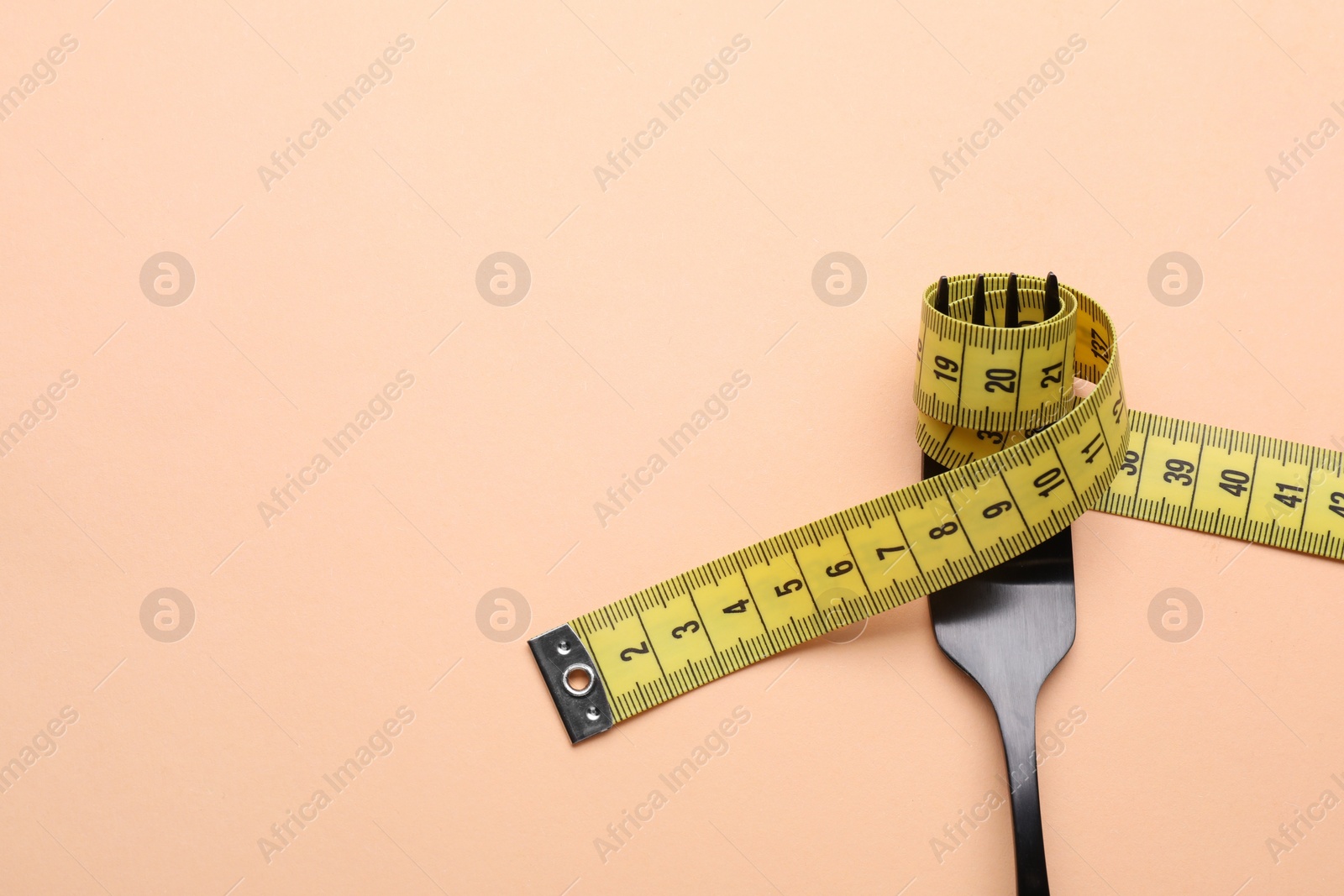 Photo of Fork with measuring tape on pale orange background, top view with space for text. Diet concept