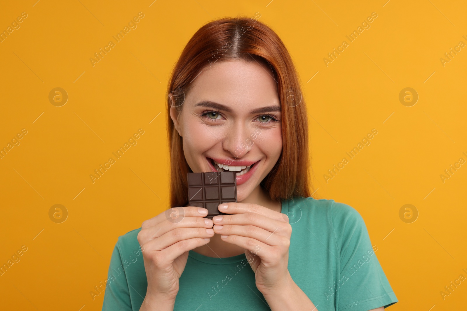 Photo of Young woman eating tasty chocolate on orange background