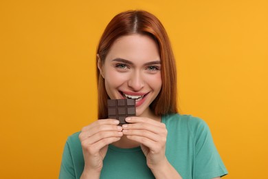 Young woman eating tasty chocolate on orange background