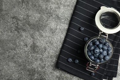 Tasty ripe blueberries in glass jar on grey table, top view. Space for text