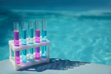 Photo of Test tubes with reagents in rack near swimming pool. Space for text