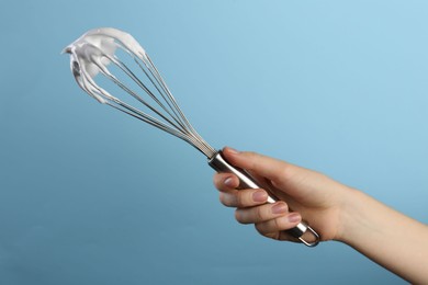 Photo of Woman holding whisk with whipped cream on light blue background, closeup