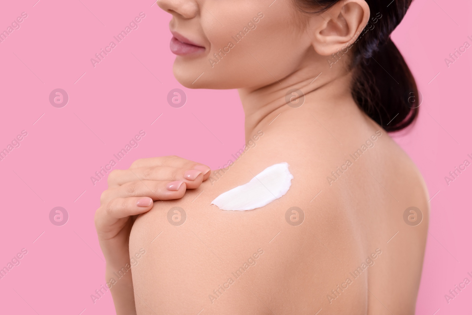 Photo of Woman with smear of body cream on her shoulder against pink background, closeup