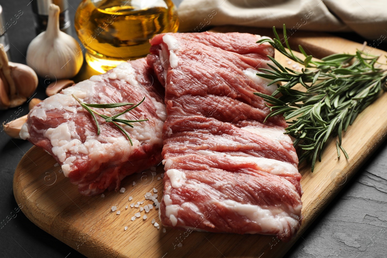 Photo of Raw ribs with rosemary and salt on black table, closeup