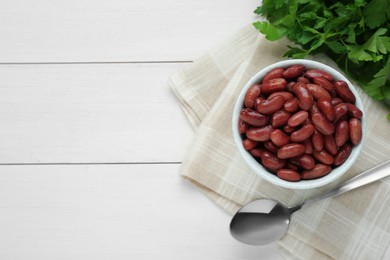 Photo of Bowl of canned kidney beans, parsley and spoon on white wooden table, top view. Space for text