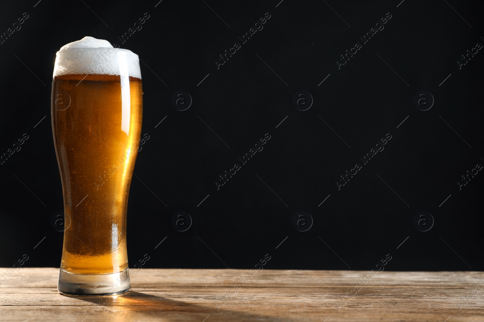 Photo of Cold tasty beer on wooden table against dark background. Space for text