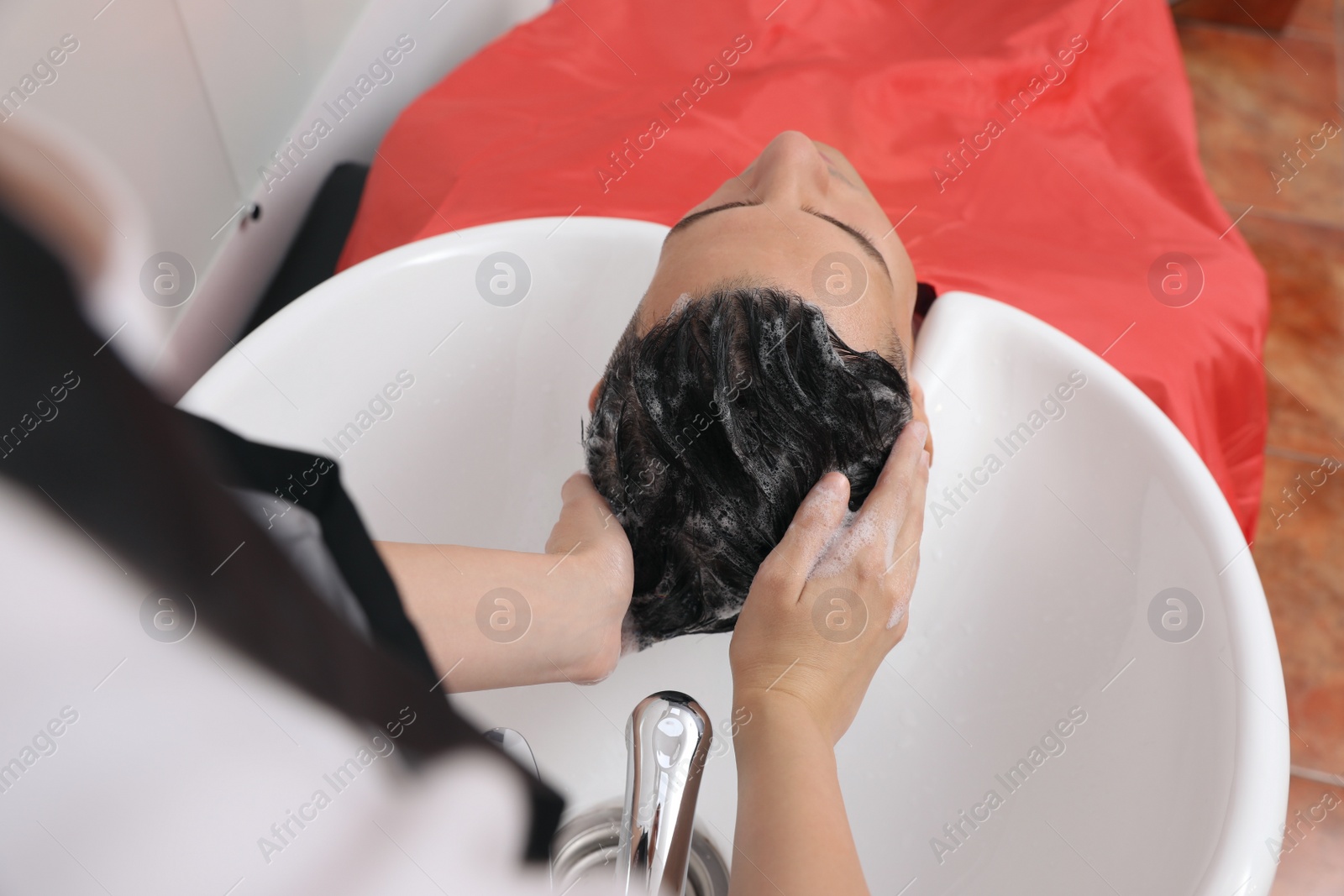 Photo of Professional hairdresser washing client's hair at sink in salon, above view